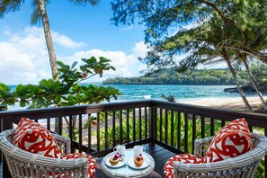 A deck with wicker chairs and a table, overlooking a beach and ocean.