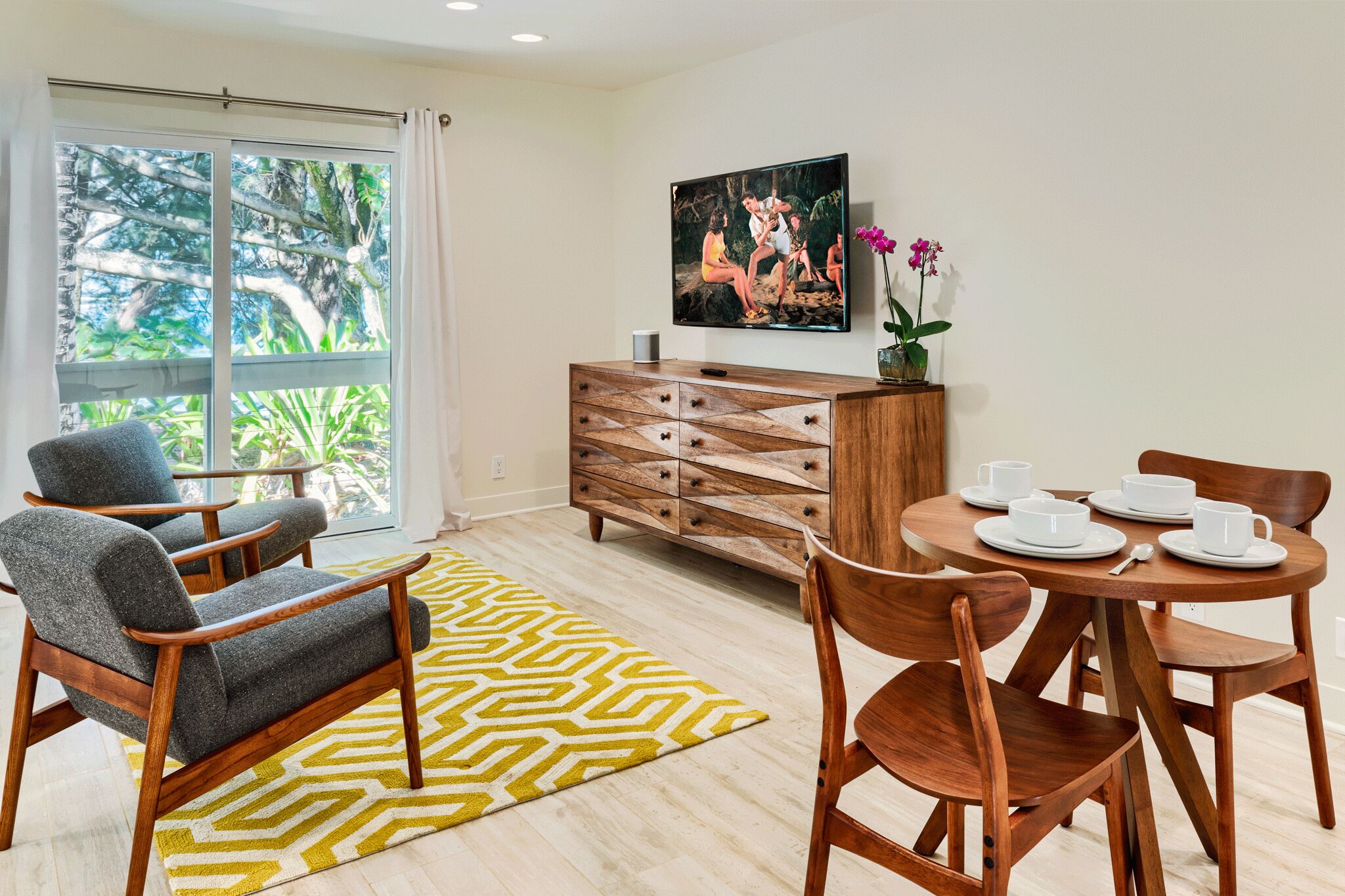 Uma sala de estar moderna com uma janela grande, uma mesa de jantar com cadeiras, um armário de madeira e um tapete estampado.