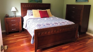 A bedroom with a wooden bed, a nightstand with a lamp, a dresser, and two landscape paintings on the walls. - Retreat-Like Setting (Trumansburg)
