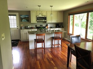 A kitchen with white cabinets, a microwave, a stove, and a sink. There are two wooden chairs and a dining table with chairs.