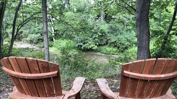 Two wooden Adirondack chairs facing a pond surrounded by dense greenery. - Retreat-Like Setting (Trumansburg)