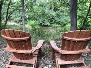 Twee houten Adirondack-stoelen gericht op een vijver, omringd door weelderige begroeiing.