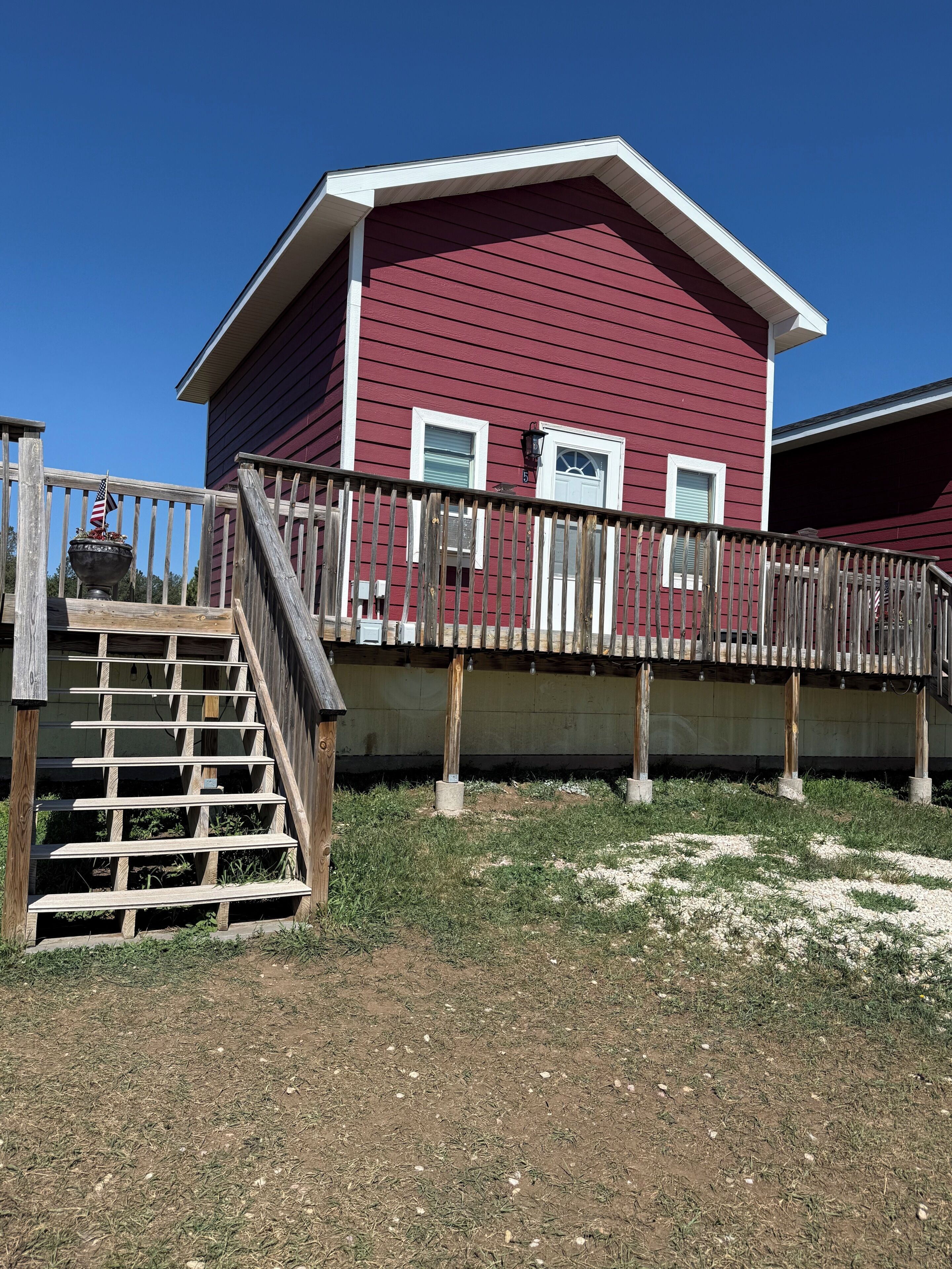 Un bâtiment rouge doté d’une terrasse en bois et d’un escalier menant à une zone abritée.