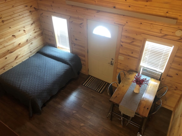 Una habitación tipo cabaña con una cama, una mesa y dos ventanas.