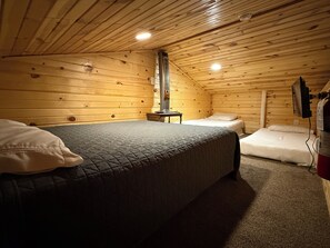 Une chambre confortable dans un chalet, avec un grand lit, un lit plus petit, un radiateur et un téléviseur fixé au mur.