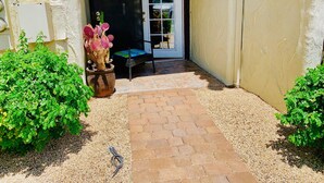 Ein überdachter Patio-Bereich mit einem Ziegelweg, der zu einer Tür mit Glasfenster führt.