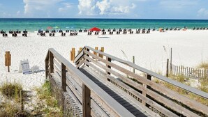 Une plage avec une promenade en bois menant au rivage, du sable blanc et une eau d’un bleu limpide.