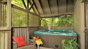 Una terraza de madera con un jacuzzi, un banco con cojín rojo y una planta en maceta.