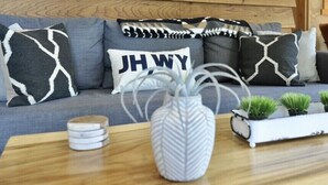 A modern living room with a grey sofa adorned with patterned cushions, a white vase with green plants, and a small white side table with decorative items. - 1B, 1B MTN. Getaway Min. from Skiing.  (Wilson)