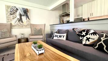 Een moderne woonkamer met een grijze bank, een houten salontafel met een plant en decoratieve kussens.