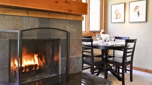 A stone fireplace with a fire, a dining table with chairs, and two framed pictures on the wall. - 1B, 1B MTN. Getaway Min. from Skiing.  (Wilson)