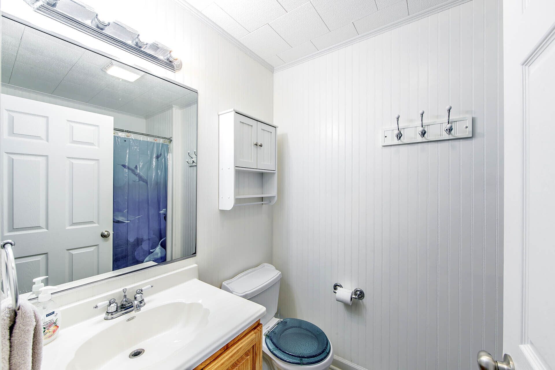 Baño con lavamanos blanco, espejo, inodoro y cortina de ducha azul.