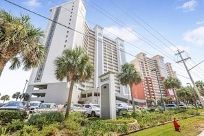 A hotel with multiple floors, a parking area, and palm trees.