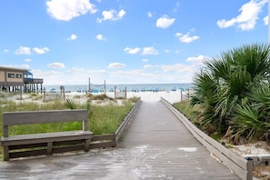 A wooden boardwalk leading to a beach with a bench on the left.