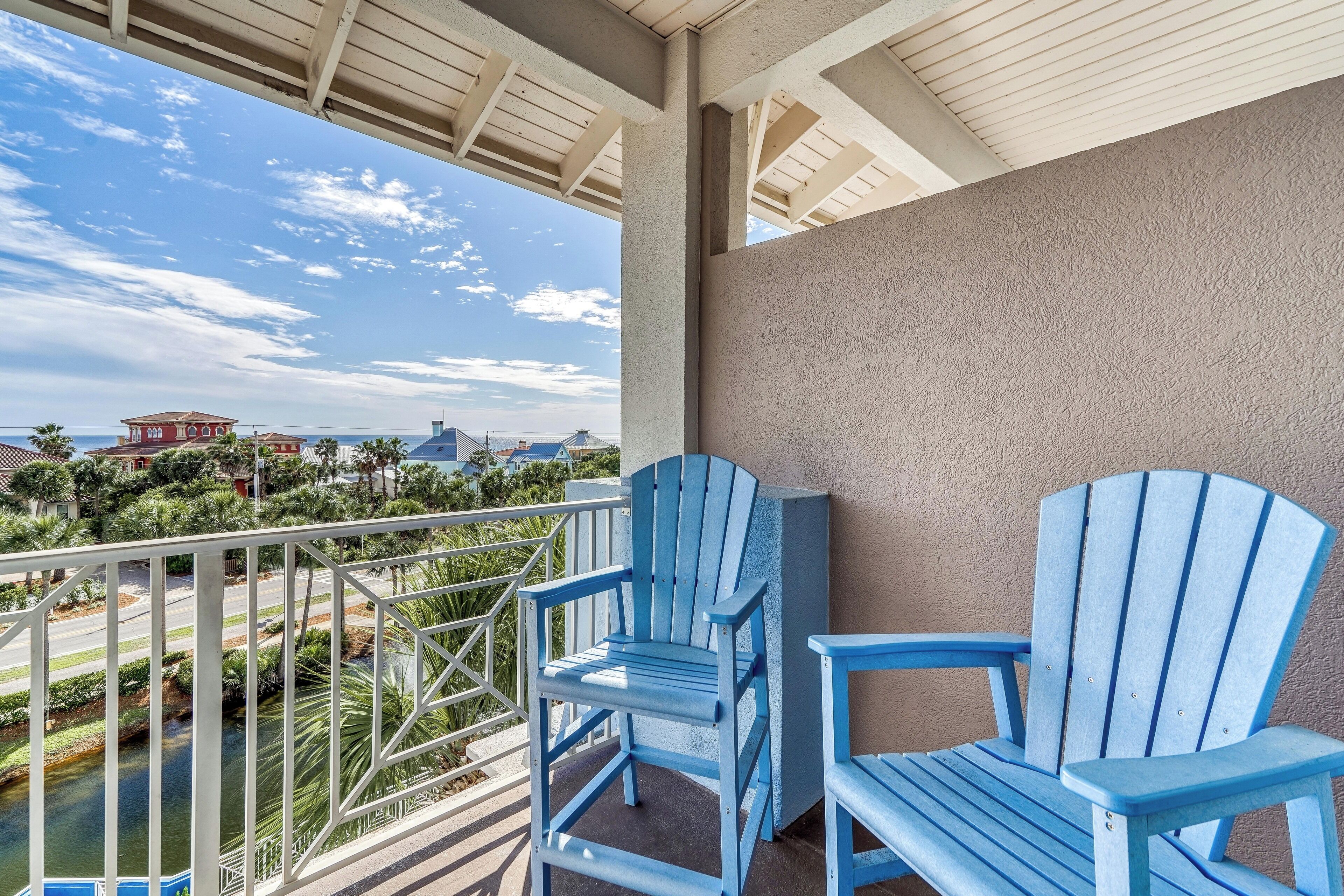 A balcony with two blue Adirondack chairs, a view of a river, and a distant building.