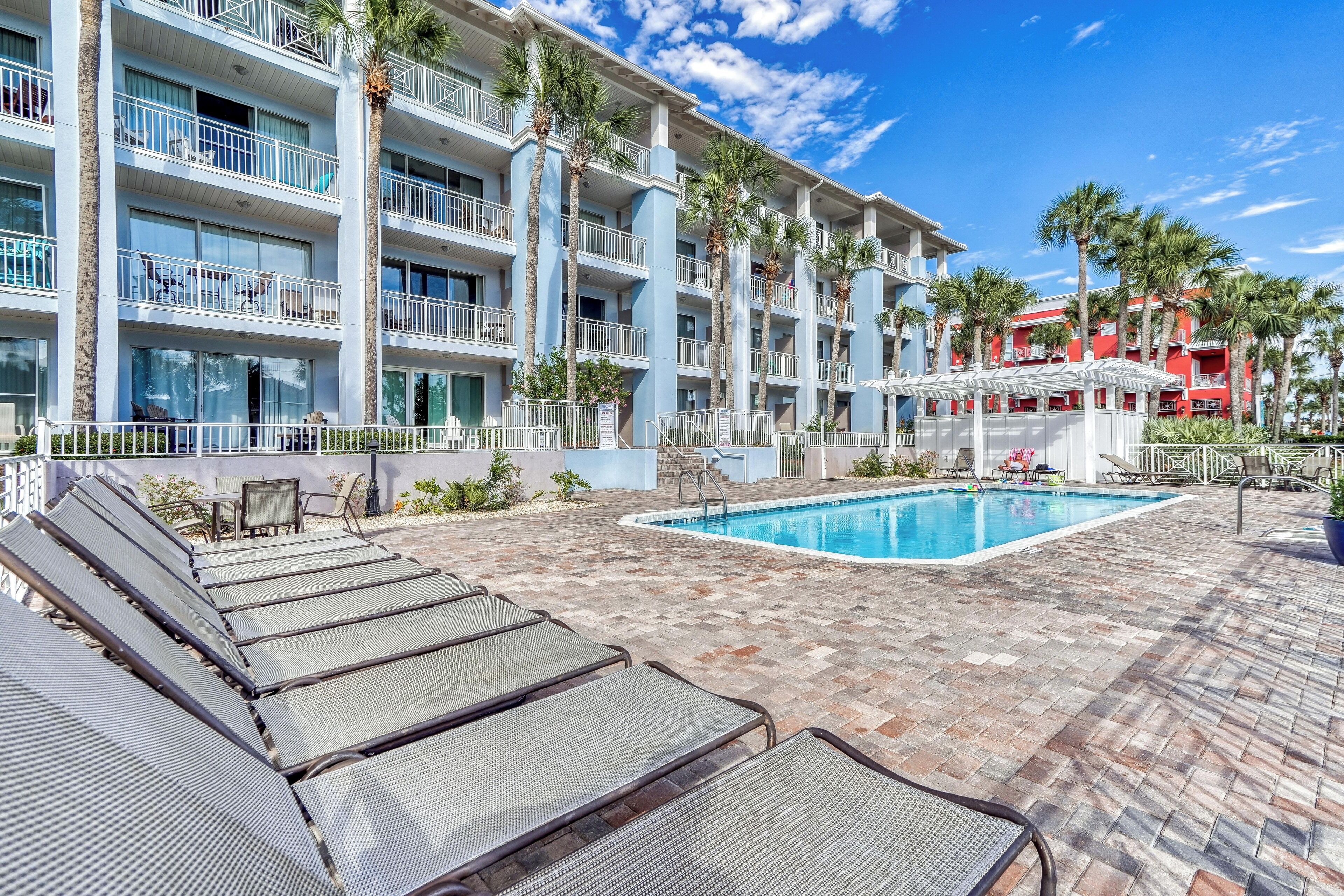 A hotel with a pool area, lounge chairs, and palm trees.