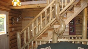 A wooden staircase with a unique design, a door with a light fixture, and a couch with a welcome sign pillow. - Welcome to 'The Log Cab-Inn' - Where Great Memories Are Made (Atlantic Mine)