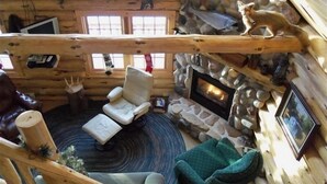 A cozy log cabin interior with a stone fireplace, a white armchair, and a rustic wooden ceiling. - Welcome to 'The Log Cab-Inn' - Where Great Memories Are Made (Atlantic Mine)