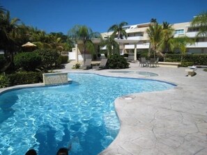A swimming pool with a curved edge, surrounded by lounge chairs and palm trees. - Paradise! Beachfront Villa with Ocean View @ Seven Seas +Wifi (Fajardo)