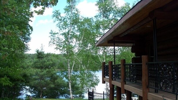A wooden building with a balcony overlooking a lake, surrounded by trees. - Custom Log Lake House on Wynne Lake  with Pontoon Boat. Summer 1 week Sat to Sat (Aurora)