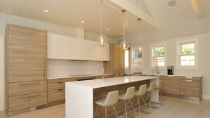 A modern kitchen with a large island, bar stools, pendant lighting, and wooden cabinetry. - Nantucket Art House - In Town ~ Heated Pool ~ Includes Guest House!  (Nantucket)
