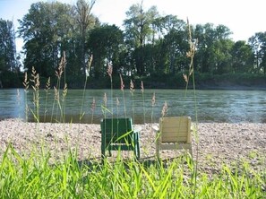 Sit by the serene lake with two comfortable chairs, surrounded by lush greenery and a tranquil atmosphere.