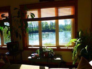 Enjoy a serene view of the river and surrounding greenery from the comfort of this room, featuring a large window and a small table with a plant.