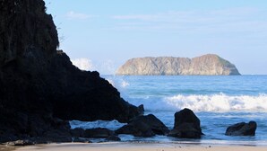 Un paysage côtier avec une rive rocheuse, des vagues qui s’écrasent contre les rochers et une île lointaine.