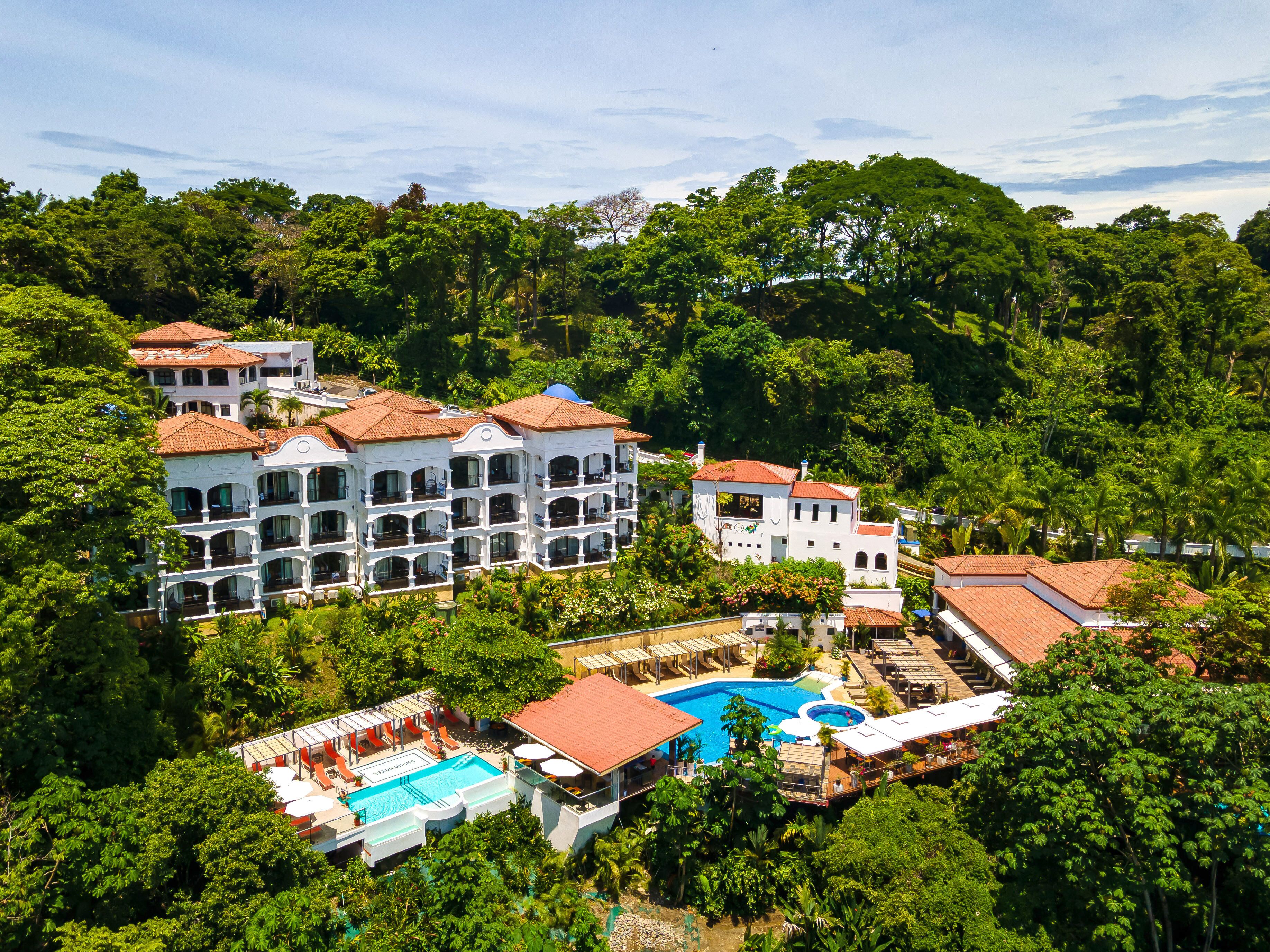 Ein Resort mit mehreren weißen Gebäuden, einem Schwimmbad und üppiger, dichter Vegetation rund um das Anwesen.