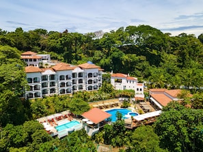 Een resort met meerdere witte gebouwen, een zwembad en weelderige begroeiing rondom het terrein.