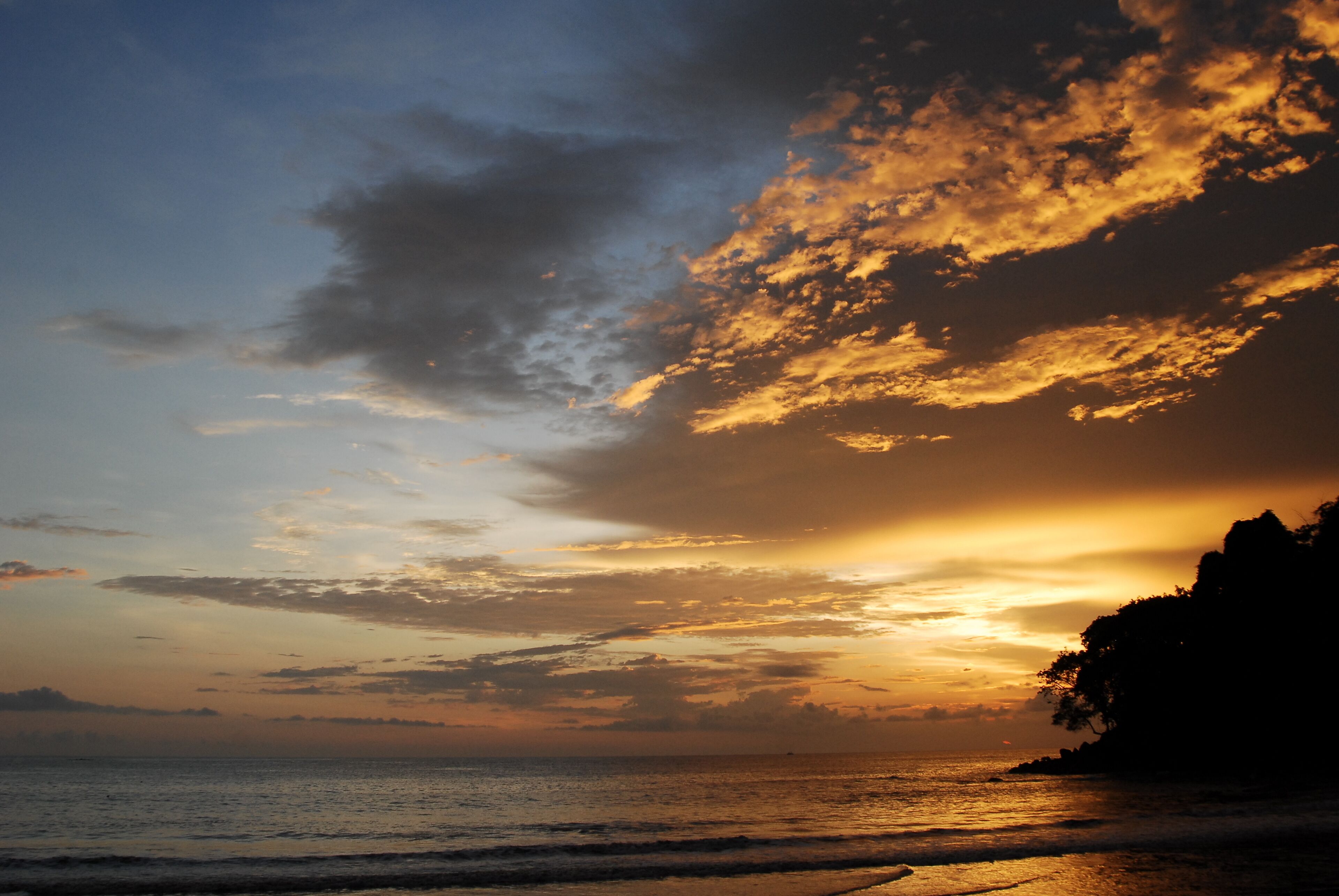 Un coucher de soleil sur une plage, avec la silhouette d'une falaise en arrière-plan.