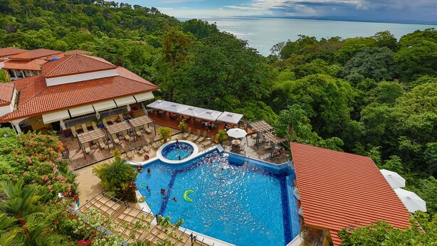 Un complexe hôtelier doté d’une piscine entourée d’une végétation luxuriante et offrant une vue sur la mer.
