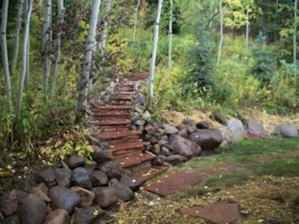 A stone pathway leading through a forested area with a series of steps ascending a small hill. - Luxurious Ski House on Snowmass Mountain. 324 Deer Ridge Lane Snowmass Village. (Snowmass Village)