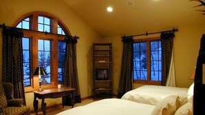 Ein Schlafzimmer mit zwei Betten, einem Schreibtisch und einem Stuhl. Große Fenster mit Vorhängen.
