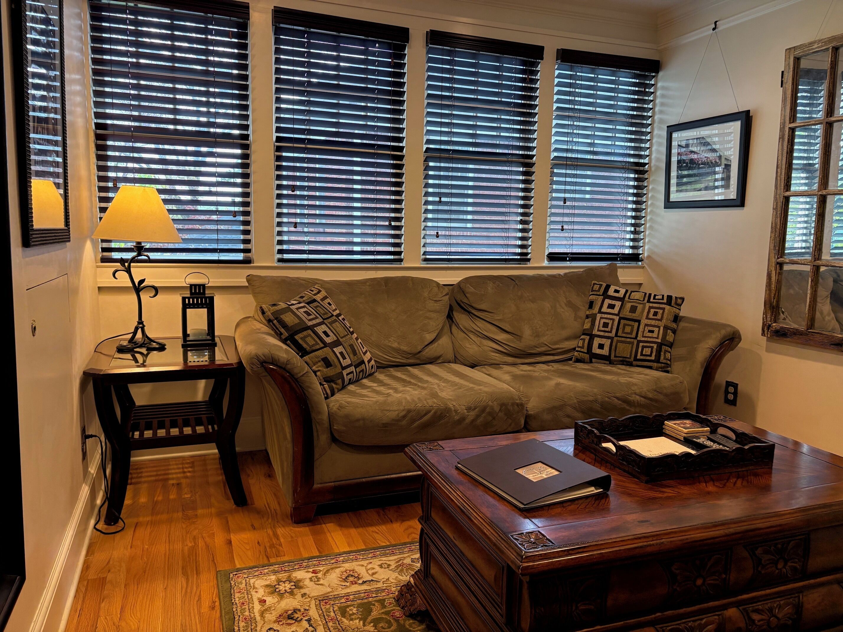 A living room with a sofa, a coffee table, a lamp, and a window with blinds.
