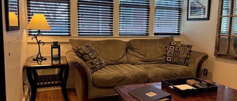 A living room with a sofa, a coffee table, a lamp, and a window with blinds.