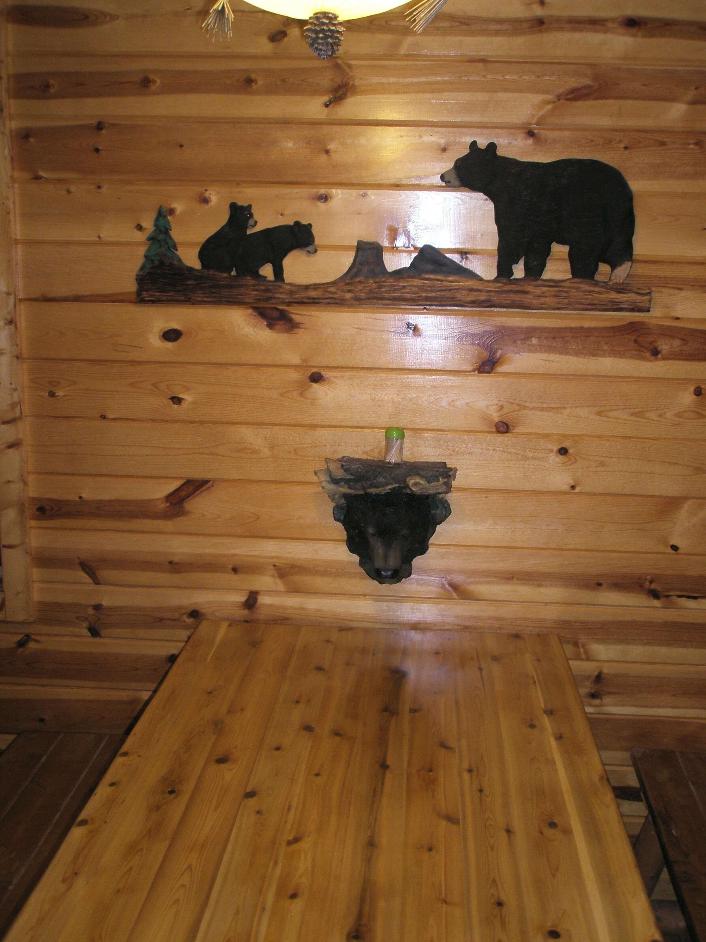 L’intérieur d’un chalet en bois, avec une tête d’ours fixée au mur, une décoration en forme de pomme de pin et un banc en bois.
