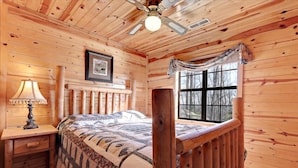 Une chambre confortable, aménagée dans un chalet en bois, avec un lit, une table de chevet, une lampe, un ventilateur de plafond et une fenêtre.