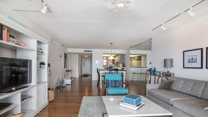 A modern living room with a flat-screen TV, a coffee table, and a sofa. There is a kitchen in the background with a dining area. - View Spectacular Sunsets from your balcony overlooking Indian Rocks Beach.  (Indian Rocks Beach)