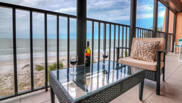 A balcony with a glass table, a wicker chair, and a bottle of wine. - View Spectacular Sunsets from your balcony overlooking Indian Rocks Beach.  (Indian Rocks Beach)