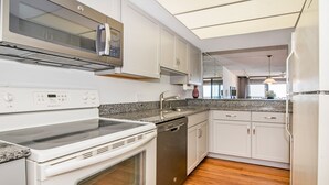 A modern kitchen with white cabinetry, a stainless steel dishwasher, a built-in oven, and a granite countertop. - View Spectacular Sunsets from your balcony overlooking Indian Rocks Beach.  (Indian Rocks Beach)
