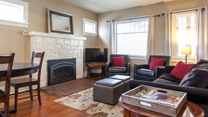 Una sala de estar con chimenea, televisor, mesa de comedor con sillas y sofá con cojines.