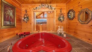Ein Holzblockhaus-Interieur mit einem herzförmigen Whirlpool, einem gerahmten Gemälde und einem Spiegel an der Wand.