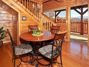 A wooden interior with a round dining table, four chairs, and a staircase leading to an outdoor deck.