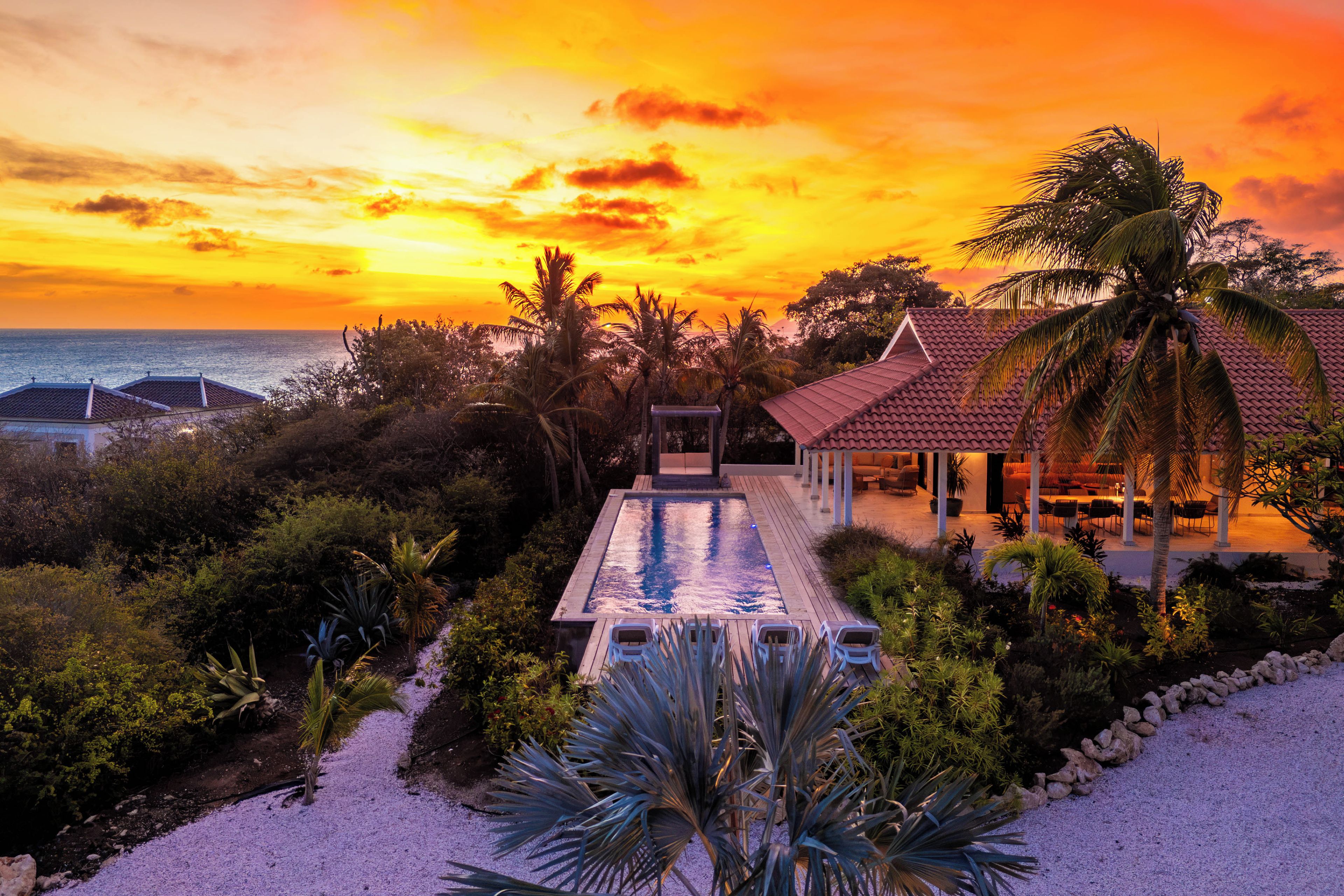 Ein Resort mit Schwimmbad, Palmen und Blick auf den Ozean bei Sonnenuntergang.