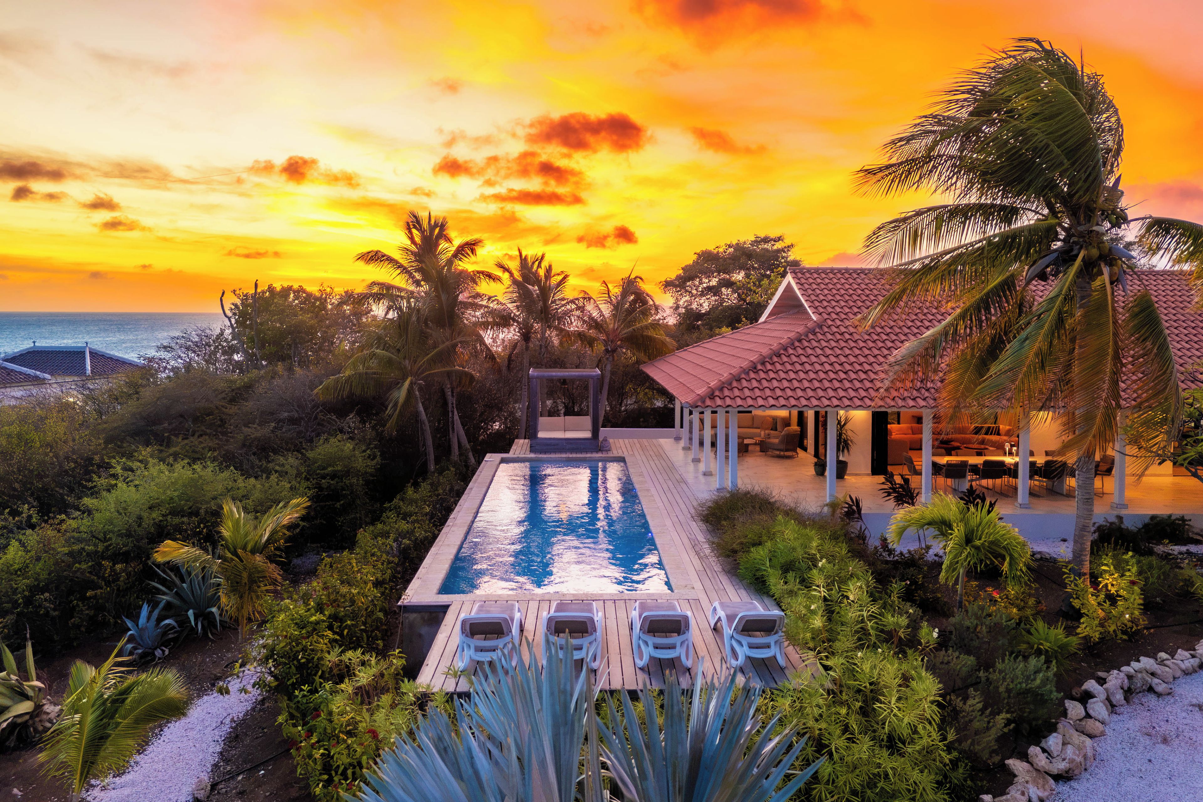 A resort with a swimming pool, lounge chairs, and a view of the ocean at sunset.