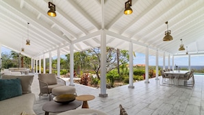 Un patio exterior techado con columnas blancas, una mesa de comedor con sillas y un sofá con cojines.