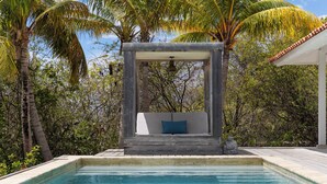 Una piscina con cubierta de madera, un banco con cojines y una estatua de piedra.