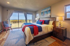 A bedroom with a large bed, a nightstand, a chair, and a painting of a beach scene.