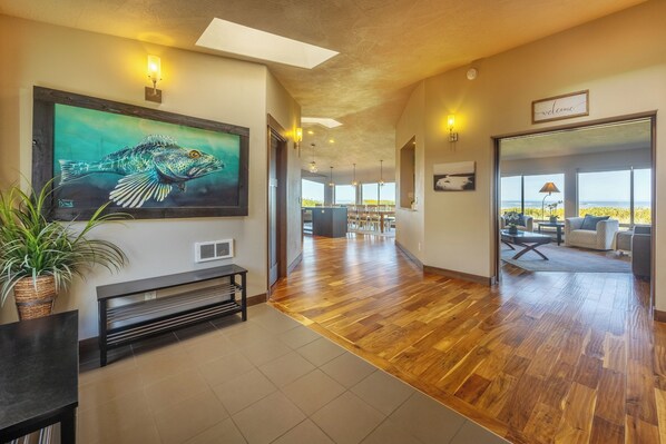 A spacious hallway with wooden flooring, a large fish painting on the wall, and a view of the outdoors through large windows.